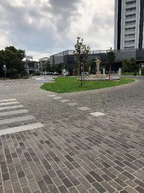 Piazza con pavimentazione in cubetti, aiuola e fontana centrale